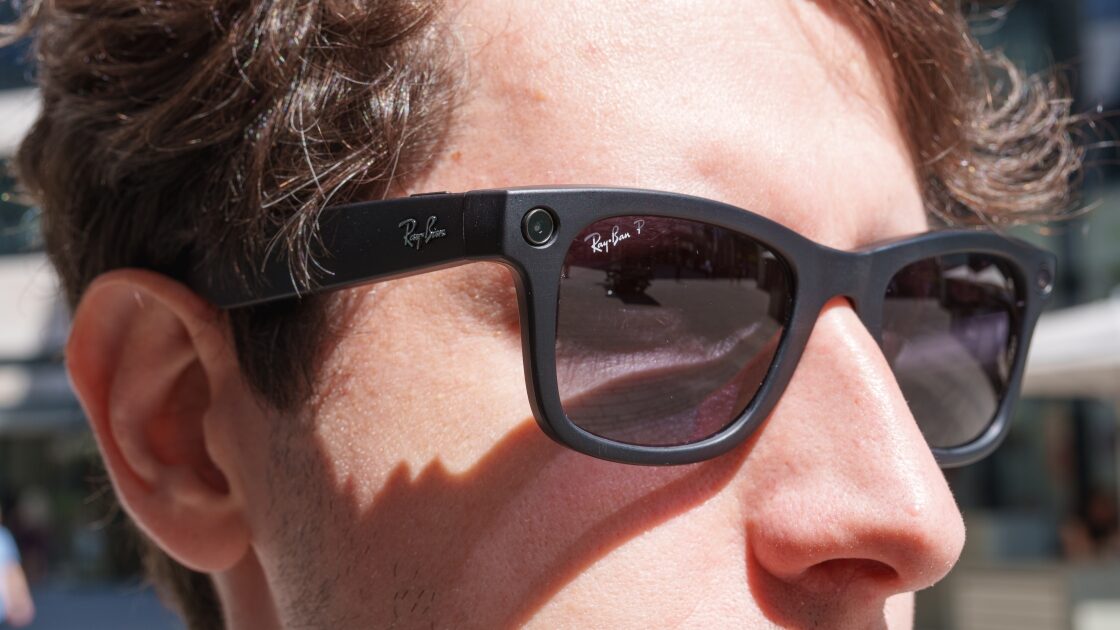 Un homme de profil porte des lunettes connectées Ray-Ban Meta en extérieur, la caméra visible sur la branche